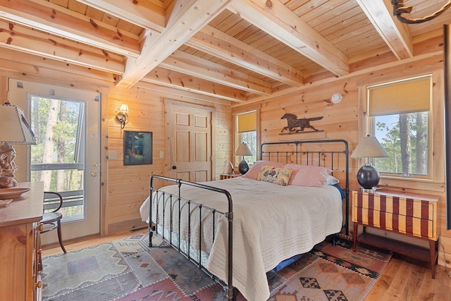 bedroom featuring beamed ceiling, multiple windows, wood finished floors, and wood walls