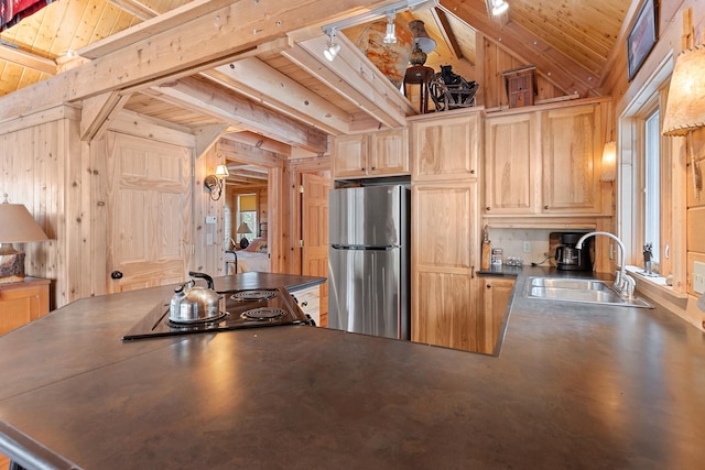 kitchen featuring wooden walls, freestanding refrigerator, light brown cabinetry, a sink, and dark countertops