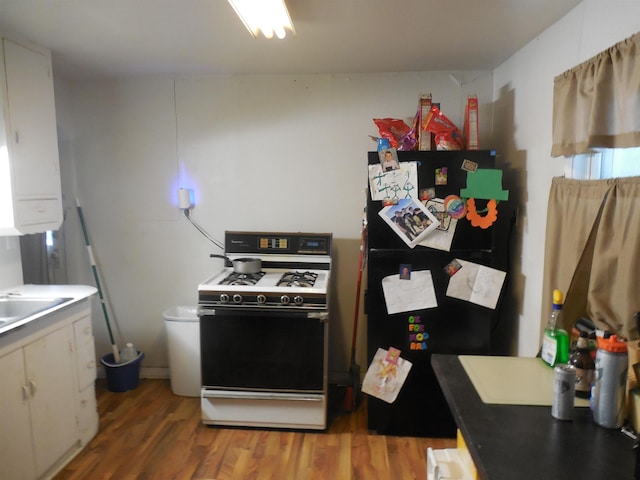 kitchen featuring light wood-style flooring, a sink, freestanding refrigerator, white cabinets, and gas range