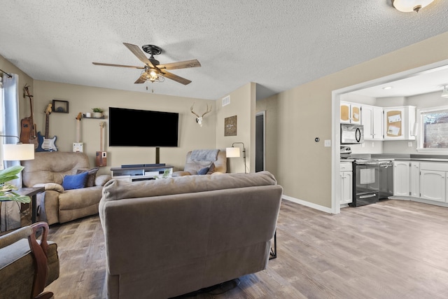 living area with light wood-style flooring, a textured ceiling, baseboards, and a ceiling fan