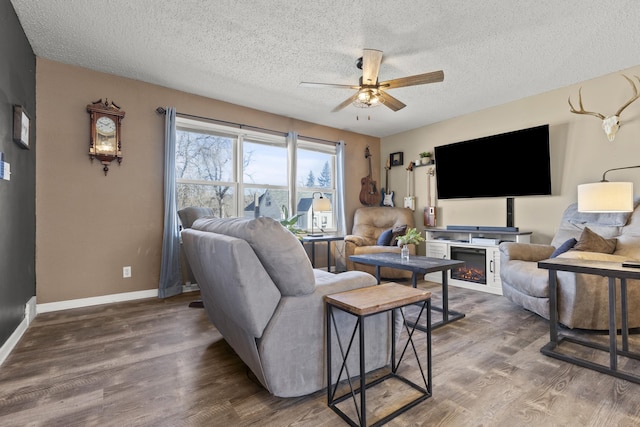 living room featuring baseboards, a lit fireplace, wood finished floors, a textured ceiling, and a ceiling fan