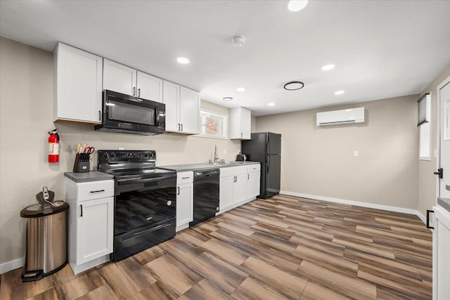 kitchen with a wall mounted air conditioner, black appliances, wood finished floors, and white cabinets