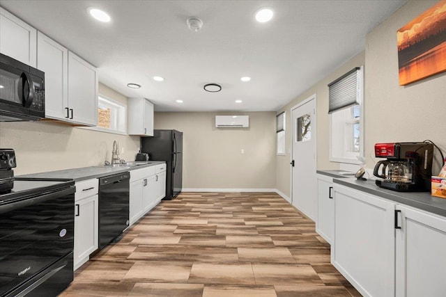 kitchen with light wood finished floors, black appliances, a wall unit AC, white cabinetry, and a sink