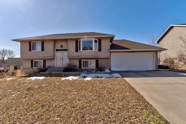 raised ranch with an attached garage, concrete driveway, and a shingled roof