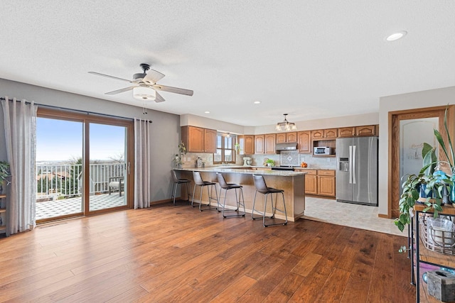 3418 Gray Fox Ct, Rapid City, SD 57701 - kitchen featuring stainless steel refrigerator with ice dispenser, under cabinet range hood, wood finished floors, a peninsula, and light countertops