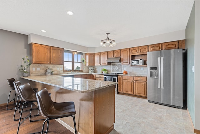 3418 Gray Fox Ct, Rapid City, SD 57701 - kitchen featuring under cabinet range hood, backsplash, appliances with stainless steel finishes, a breakfast bar area, and a peninsula