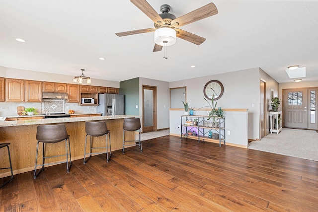 3418 Gray Fox Ct, Rapid City, SD 57701 - kitchen featuring under cabinet range hood, stainless steel appliances, wood-type flooring, and backsplash