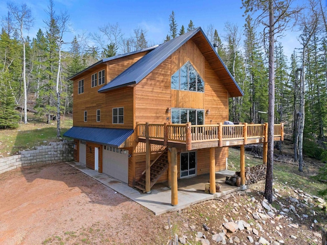 view of front facade with a deck, an attached garage, dirt driveway, and metal roof