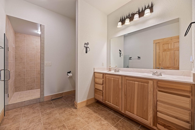 full bathroom featuring double vanity, tiled shower, baseboards, and a sink