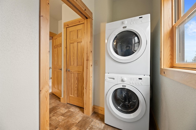 clothes washing area with laundry area, stone finish flooring, stacked washer / drying machine, and baseboards