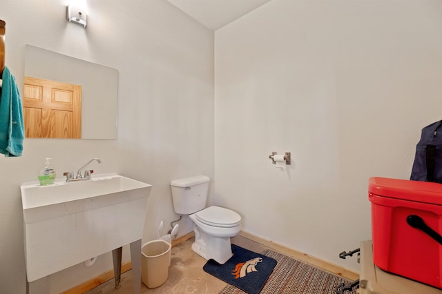 bathroom with toilet, baseboards, concrete floors, and a sink