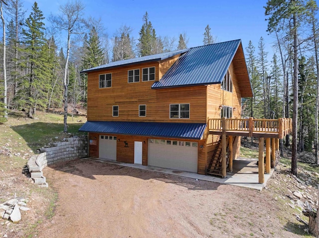 rustic home featuring an attached garage, stairs, dirt driveway, a deck, and metal roof