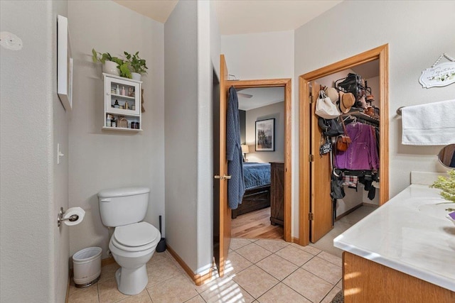 bathroom featuring vanity, baseboards, a walk in closet, tile patterned floors, and toilet