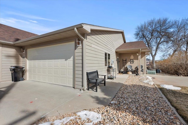 view of side of home featuring a patio, concrete driveway, a garage, and a shingled roof