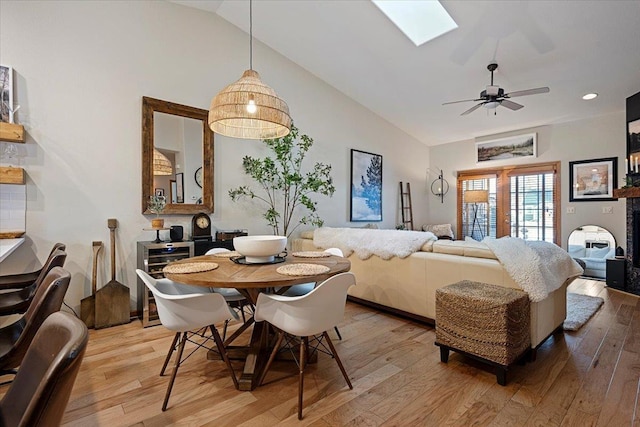 dining area with ceiling fan, high vaulted ceiling, a skylight, and light wood finished floors