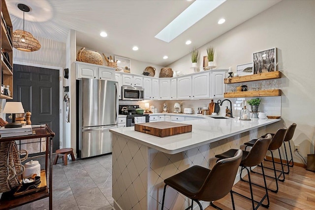 kitchen featuring a kitchen bar, a peninsula, white cabinets, stainless steel appliances, and a sink