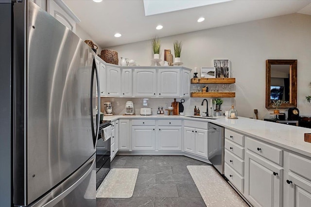 kitchen with vaulted ceiling with skylight, a sink, white cabinets, appliances with stainless steel finishes, and tasteful backsplash