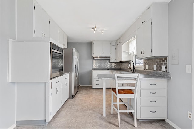 kitchen featuring stainless steel refrigerator with ice dispenser, a sink, under cabinet range hood, tasteful backsplash, and baseboards