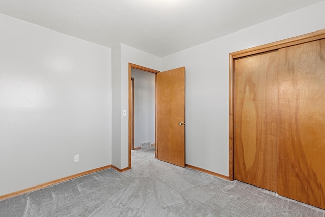 unfurnished bedroom featuring visible vents, baseboards, a closet, and light carpet