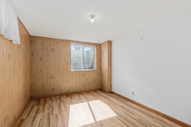 empty room featuring wood walls, baseboards, and light wood-style floors