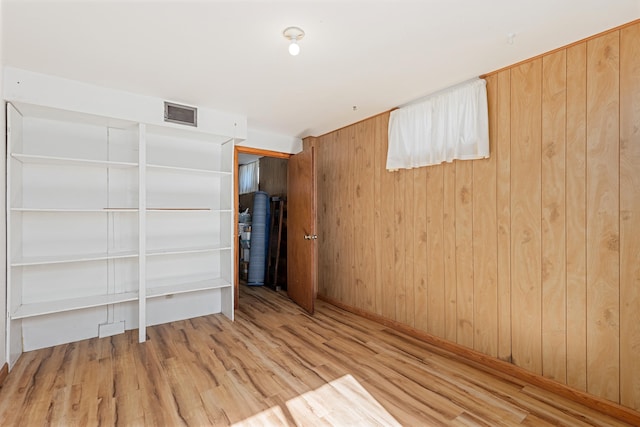 unfurnished room with visible vents, wooden walls, and wood finished floors