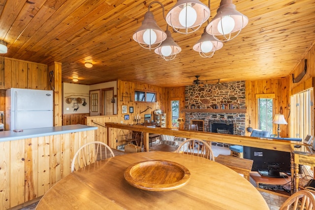 dining space with wooden walls, a fireplace, wooden ceiling, and a ceiling fan