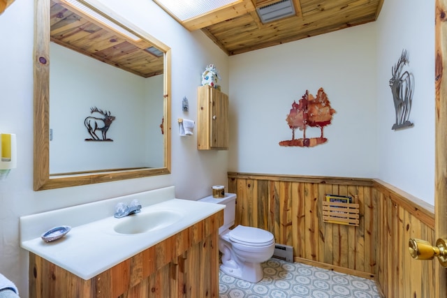 bathroom with toilet, a baseboard heating unit, wooden ceiling, wainscoting, and vanity