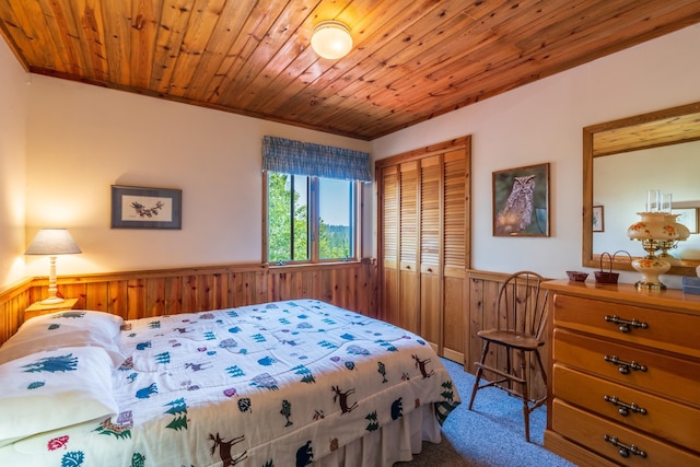 carpeted bedroom with wooden ceiling, wooden walls, a closet, and wainscoting