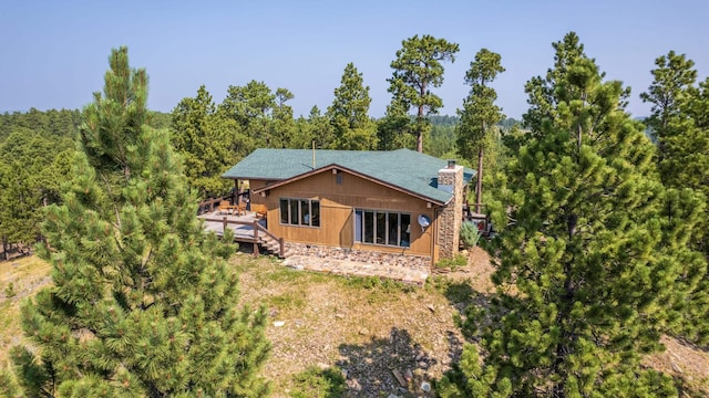 rear view of house featuring a wooden deck, a forest view, and a chimney