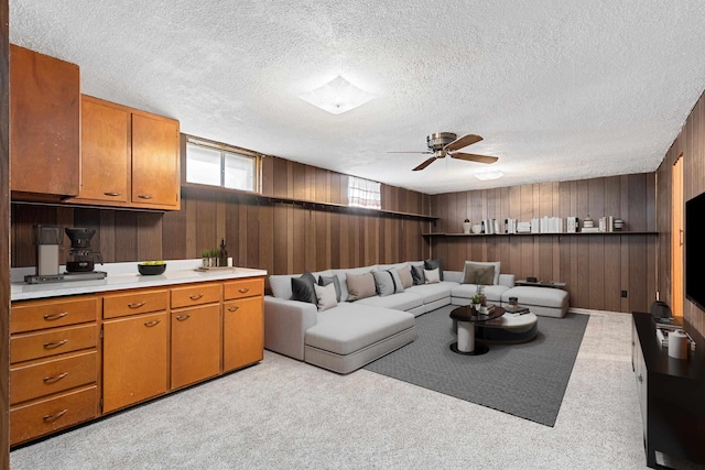 living room featuring ceiling fan, light colored carpet, wood walls, and a textured ceiling