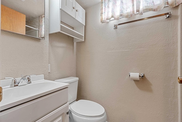 bathroom featuring toilet, walk in shower, vanity, and a textured wall