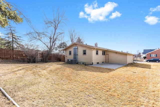 rear view of house with a lawn, central AC, fence, a chimney, and a patio area