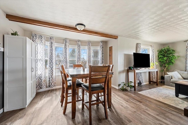 dining space featuring beam ceiling, baseboards, light wood-type flooring, and a textured ceiling