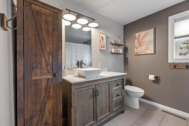 bathroom featuring visible vents, toilet, a textured ceiling, baseboards, and vanity