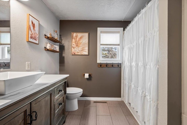 full bath with visible vents, toilet, a textured ceiling, baseboards, and vanity