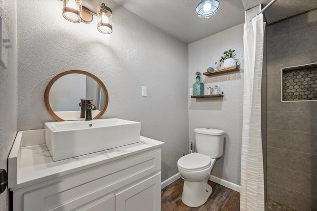 full bathroom featuring baseboards, toilet, tiled shower, wood finished floors, and vanity