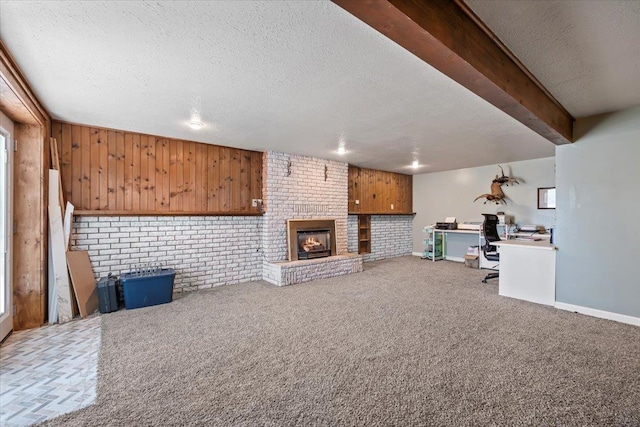 unfurnished living room featuring a brick fireplace, baseboards, carpet, beam ceiling, and a textured ceiling