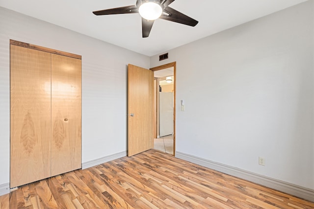 unfurnished bedroom featuring light wood finished floors, visible vents, baseboards, freestanding refrigerator, and a closet