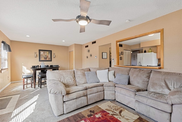 living room with baseboards, light carpet, a textured ceiling, and a ceiling fan