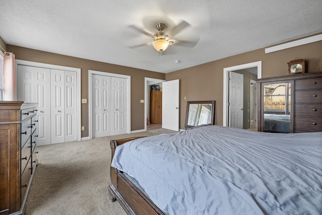 carpeted bedroom featuring baseboards, a textured ceiling, two closets, and a ceiling fan