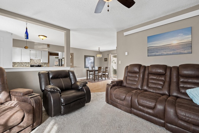 living area featuring baseboards, a textured ceiling, light wood-style floors, and ceiling fan