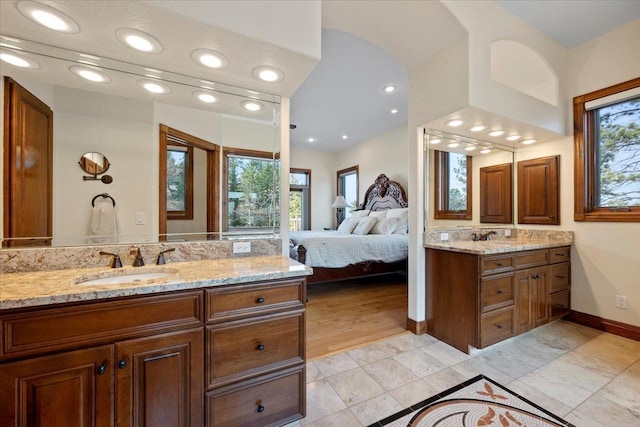 ensuite bathroom with two vanities, baseboards, connected bathroom, and a sink