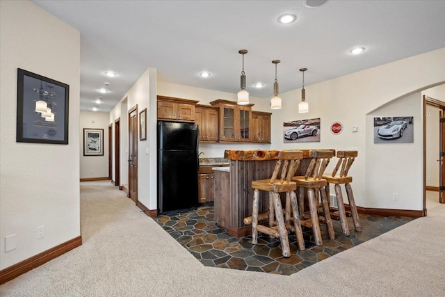 kitchen featuring dark carpet, freestanding refrigerator, arched walkways, brown cabinetry, and glass insert cabinets