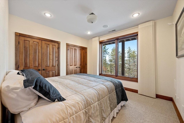 bedroom with visible vents, baseboards, multiple closets, light carpet, and recessed lighting