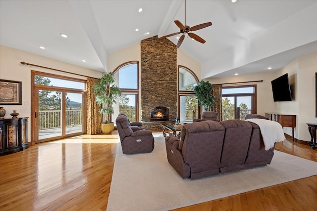 living area with a wealth of natural light, a stone fireplace, light wood-style flooring, and high vaulted ceiling