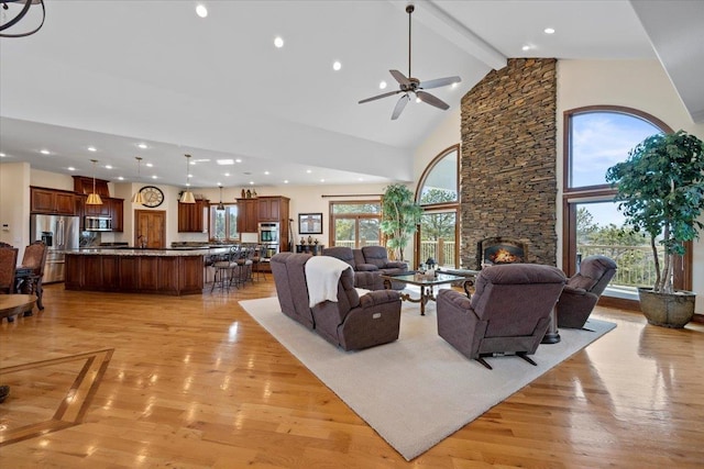 living area featuring beamed ceiling, light wood-style flooring, a fireplace, and a healthy amount of sunlight