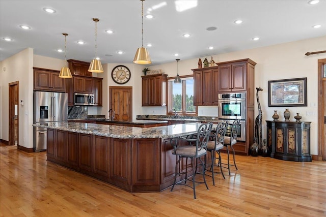 kitchen featuring recessed lighting, a large island with sink, a sink, light wood-style floors, and appliances with stainless steel finishes