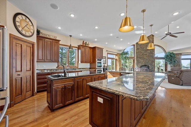 kitchen featuring a spacious island, light wood finished floors, a stone fireplace, a ceiling fan, and a sink