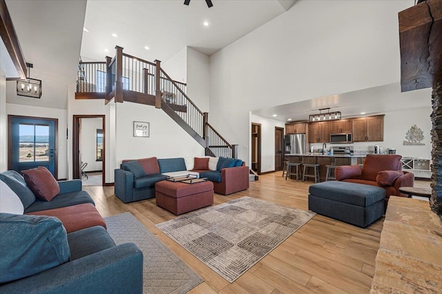 living room featuring stairway, a high ceiling, a chandelier, and light wood finished floors