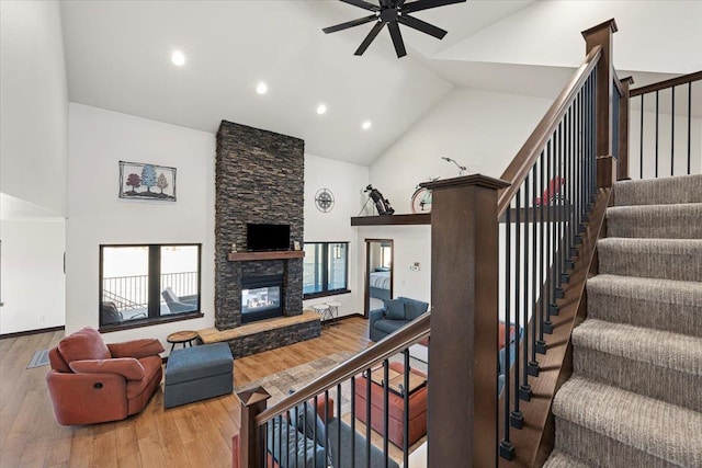 living area with a stone fireplace, wood finished floors, a ceiling fan, and high vaulted ceiling